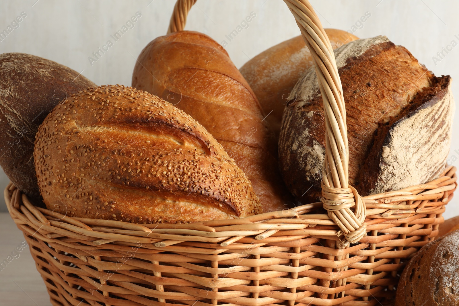 Photo of Different freshly baked breads in wicker basket on table, closeup