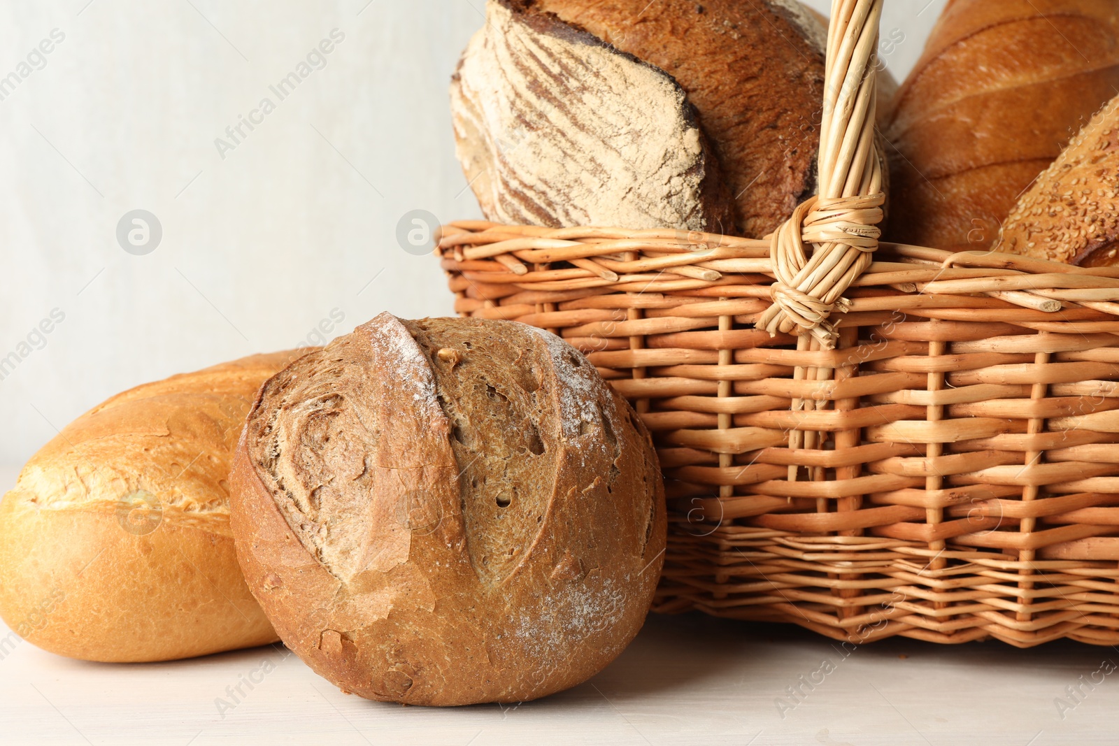 Photo of Different freshly baked breads and wicker basket on white wooden table, closeup