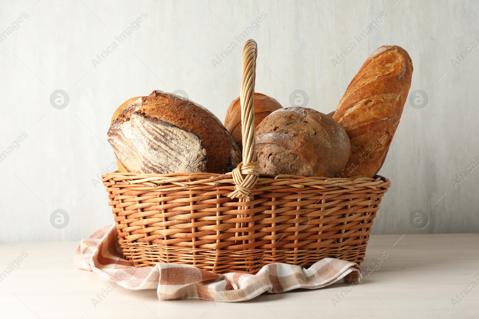 Photo of Different freshly baked breads in wicker basket on white wooden table, closeup