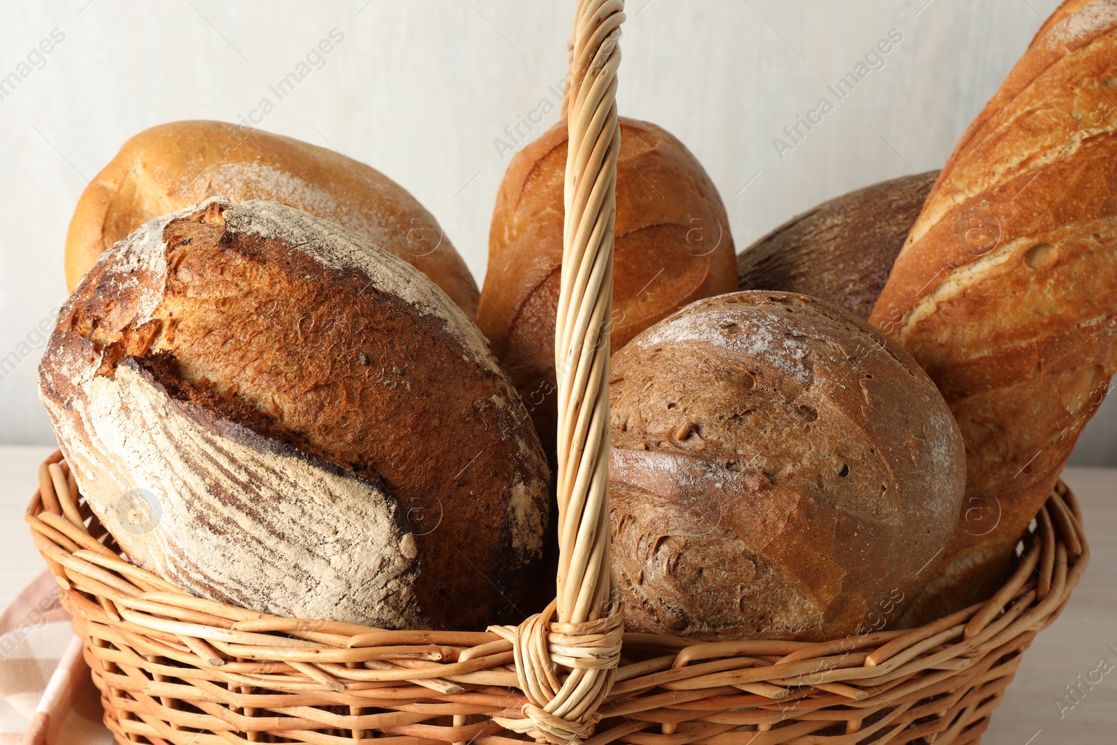 Photo of Different freshly baked breads in wicker basket on table, closeup