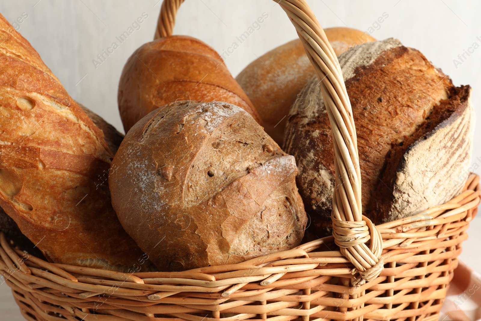 Photo of Different freshly baked breads in wicker basket on table, closeup