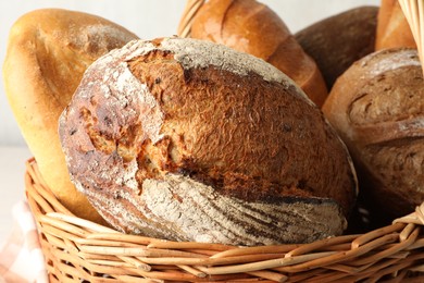 Photo of Different freshly baked breads in wicker basket on table, closeup