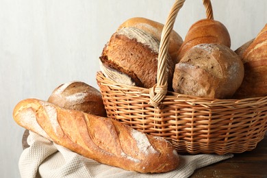 Photo of Different freshly baked breads and wicker basket on wooden table, closeup