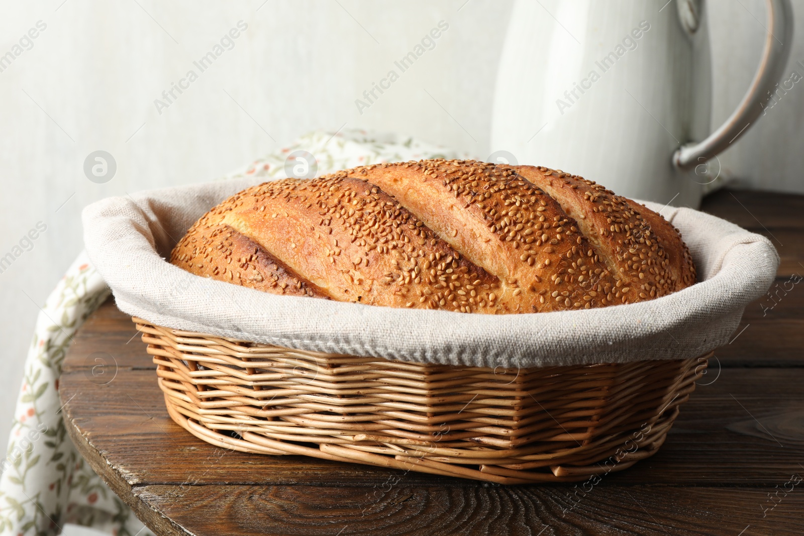 Photo of Freshly baked bread with sesame seeds in wicker basket on wooden table, closeup