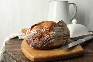 Photo of Freshly baked bread and knife on wooden table, closeup