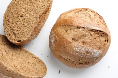 Photo of Whole and halves of freshly baked bread on white background, flat lay