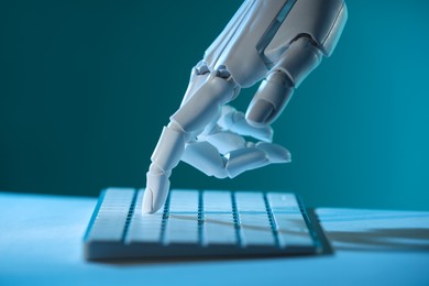 Photo of Artificial intelligence. Robot hand using keyboard at table in blue light, closeup