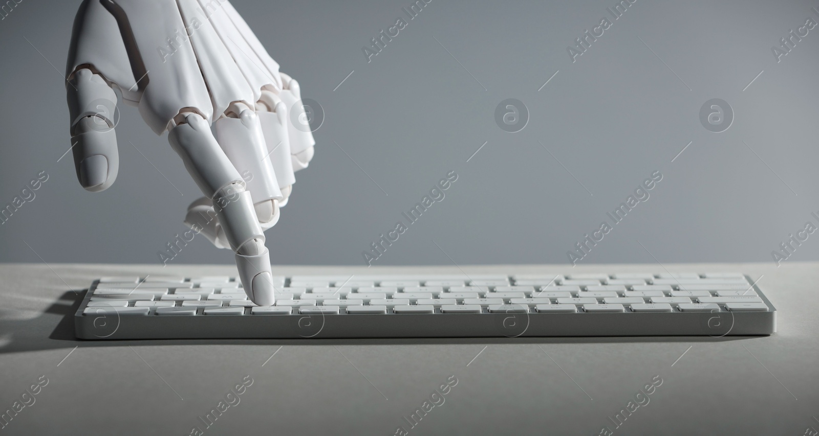 Photo of Artificial intelligence. Robot hand using keyboard at light table against grey background, closeup