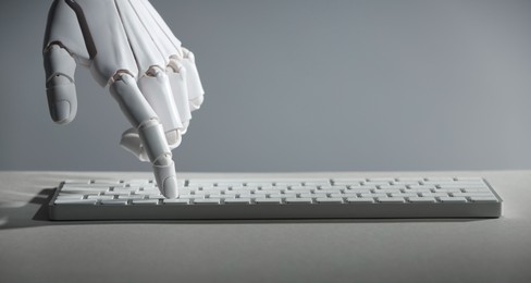 Photo of Artificial intelligence. Robot hand using keyboard at light table against grey background, closeup