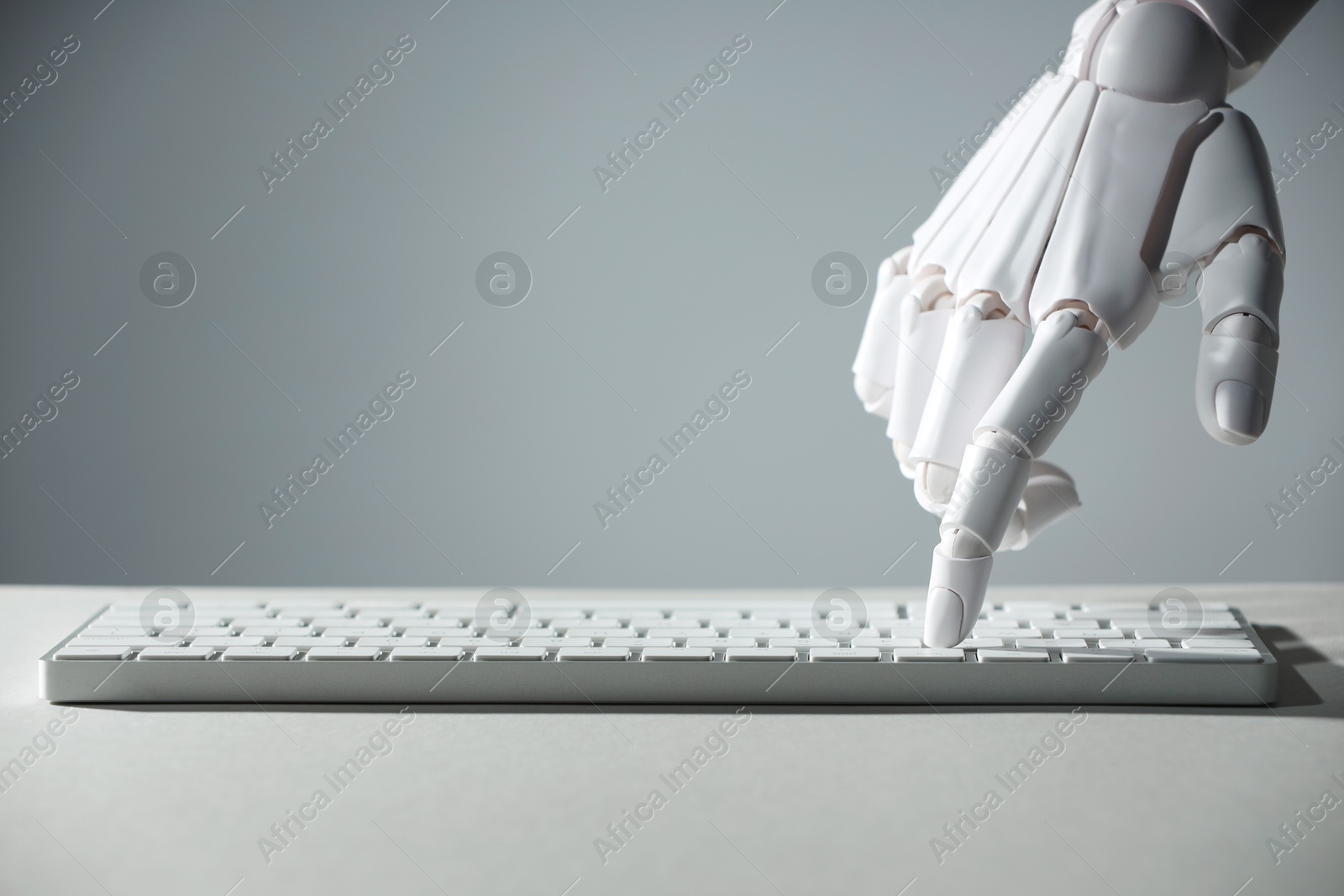 Photo of Artificial intelligence. Robot hand using keyboard at light table against grey background, closeup