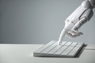 Photo of Artificial intelligence. Robot hand using keyboard at light table against grey background, closeup. Space for text