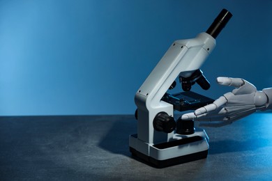 Photo of Artificial intelligence. Robot hand working with microscope at grey table against blue background, space for text