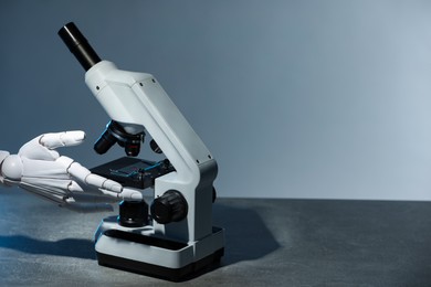 Photo of Artificial intelligence. Robot hand working with microscope at table against light grey background, space for text