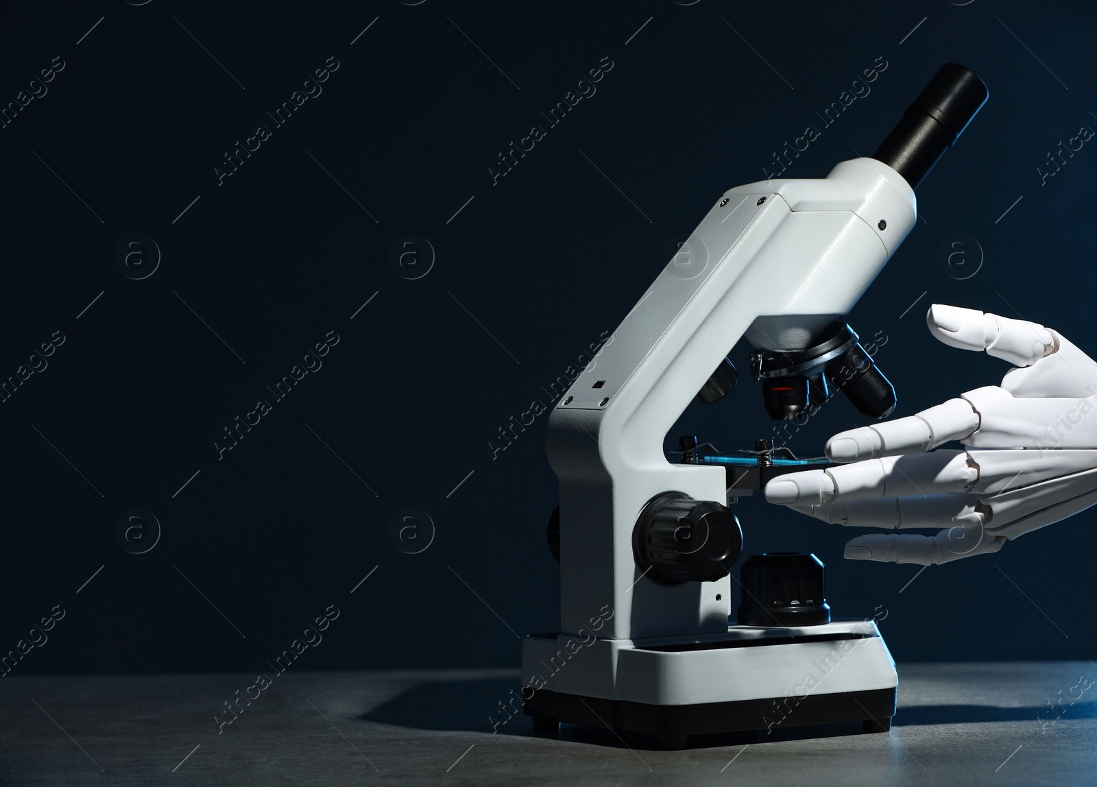 Photo of Artificial intelligence. Robot hand working with microscope at grey table against dark blue background, space for text