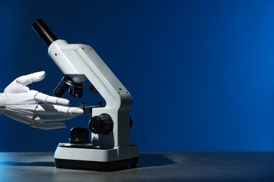 Photo of Artificial intelligence. Robot hand working with microscope at table against blue background, space for text