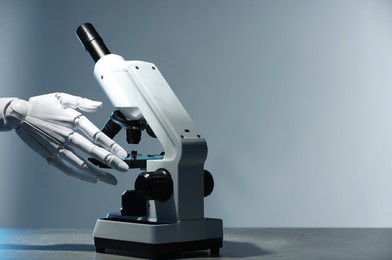 Photo of Artificial intelligence. Robot hand working with microscope at table against light grey background, space for text