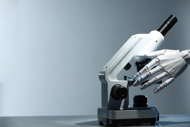 Photo of Artificial intelligence. Robot hand working with microscope at table against light grey background, space for text