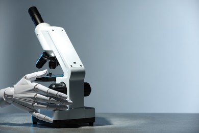 Photo of Artificial intelligence. Robot hand working with microscope at table against light grey background, space for text