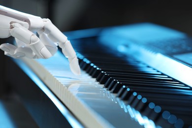 Photo of Artificial intelligence. Robot hand playing piano on dark background, closeup