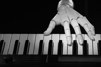 Photo of Artificial intelligence. Robot hand playing synthesizer on black background, closeup