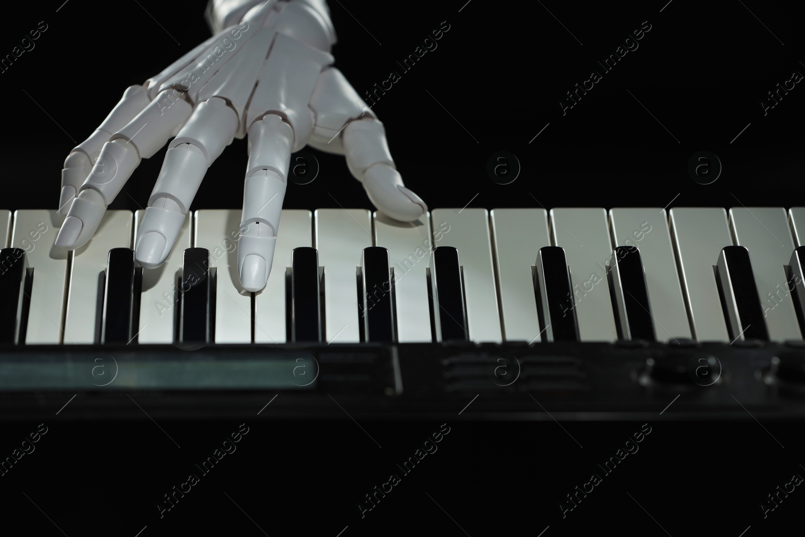 Photo of Artificial intelligence. Robot hand playing synthesizer on black background, closeup