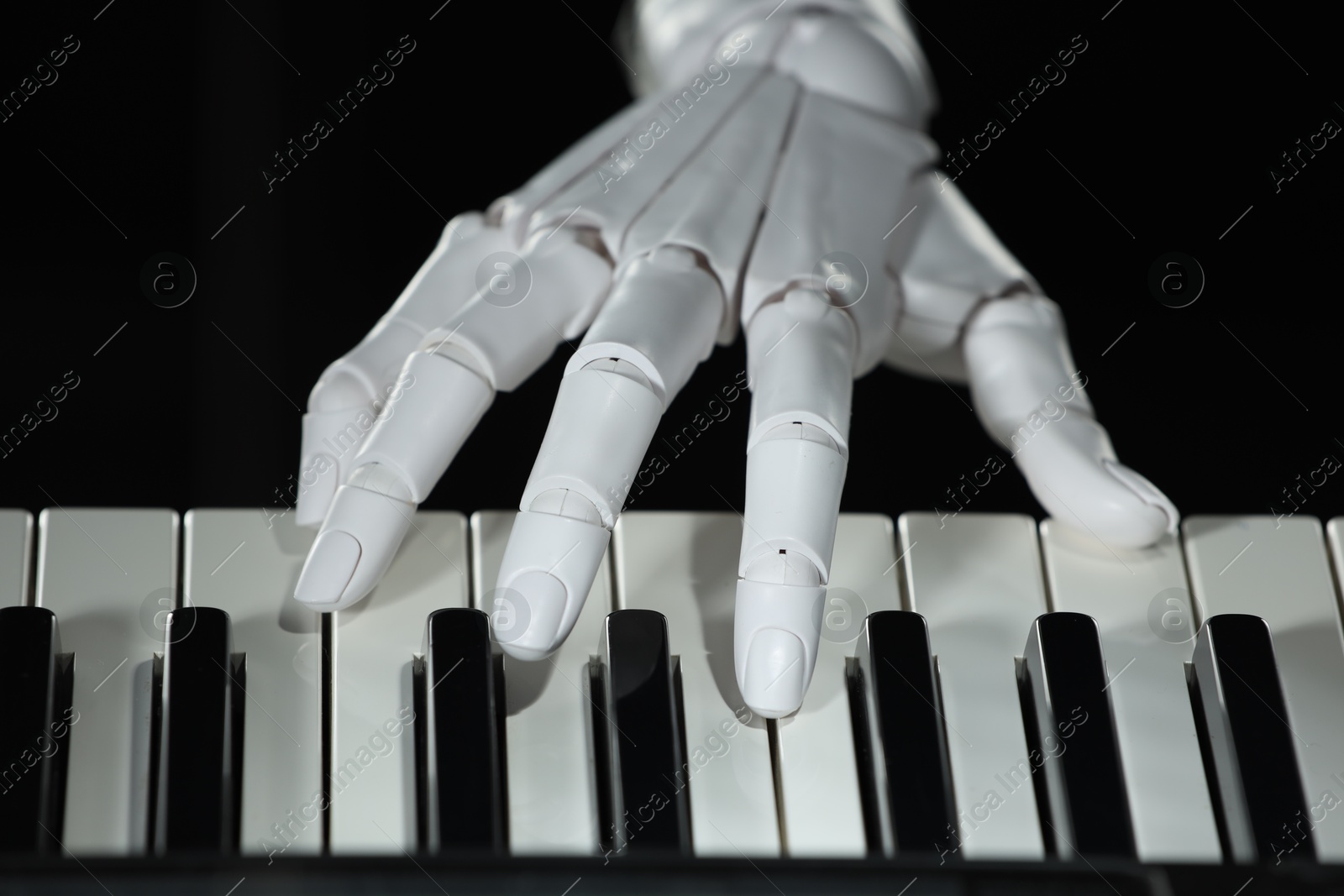 Photo of Artificial intelligence. Robot hand playing piano on black background, closeup