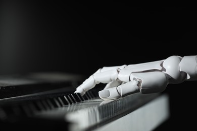 Photo of Artificial intelligence. Robot hand playing piano on black background, closeup