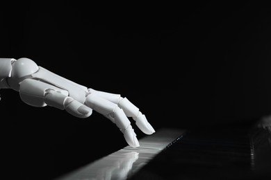 Photo of Artificial intelligence. Robot hand playing piano on black background, closeup