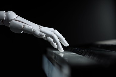 Photo of Artificial intelligence. Robot hand playing piano on black background, closeup