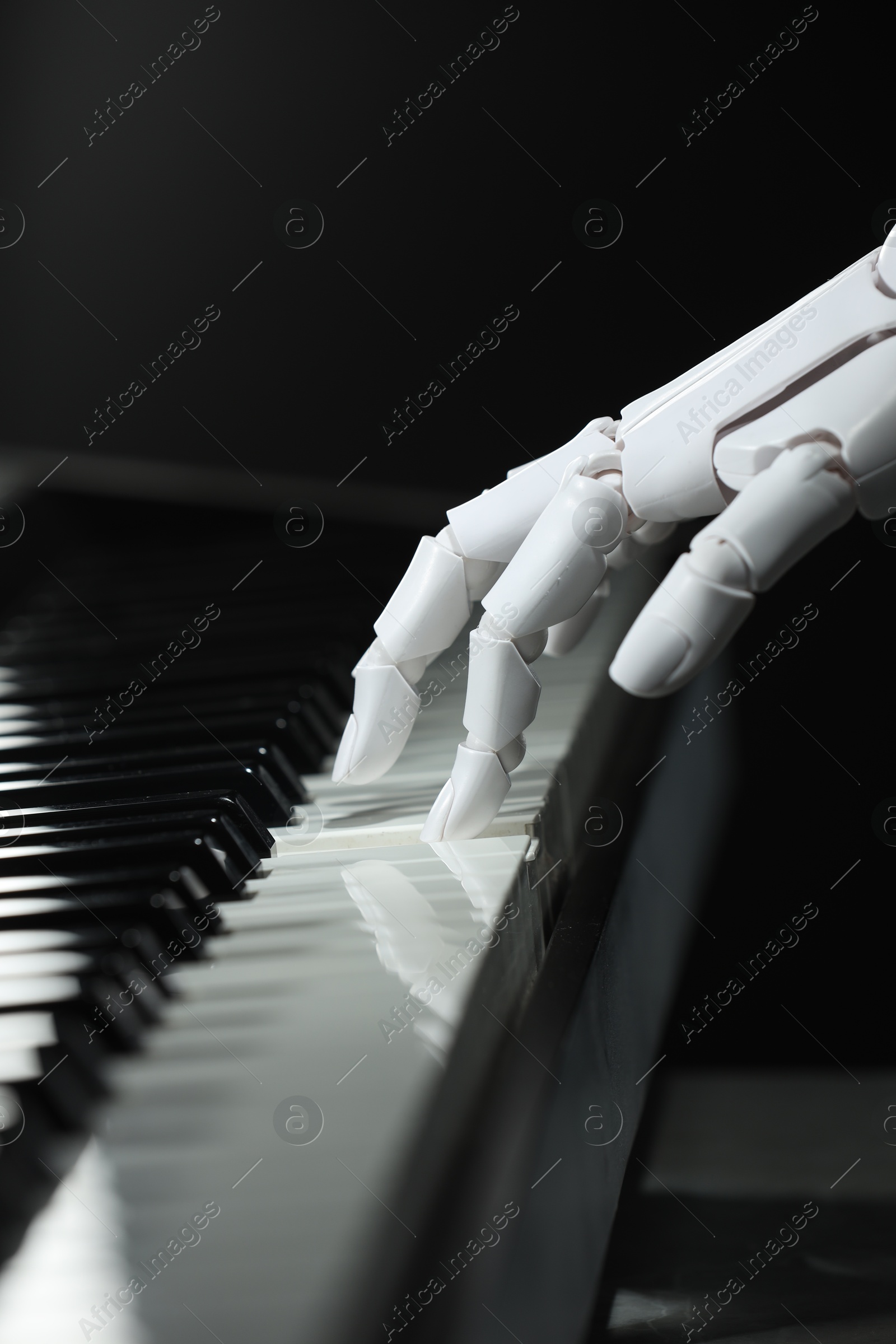 Photo of Artificial intelligence. Robot hand playing piano on black background, closeup