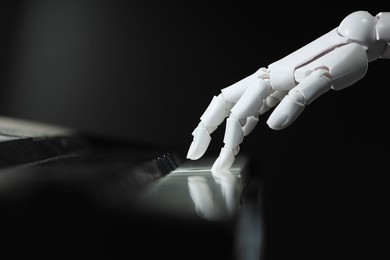 Photo of Artificial intelligence. Robot hand playing piano on black background, closeup