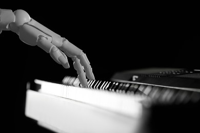 Photo of Artificial intelligence. Robot hand playing synthesizer on black background, closeup