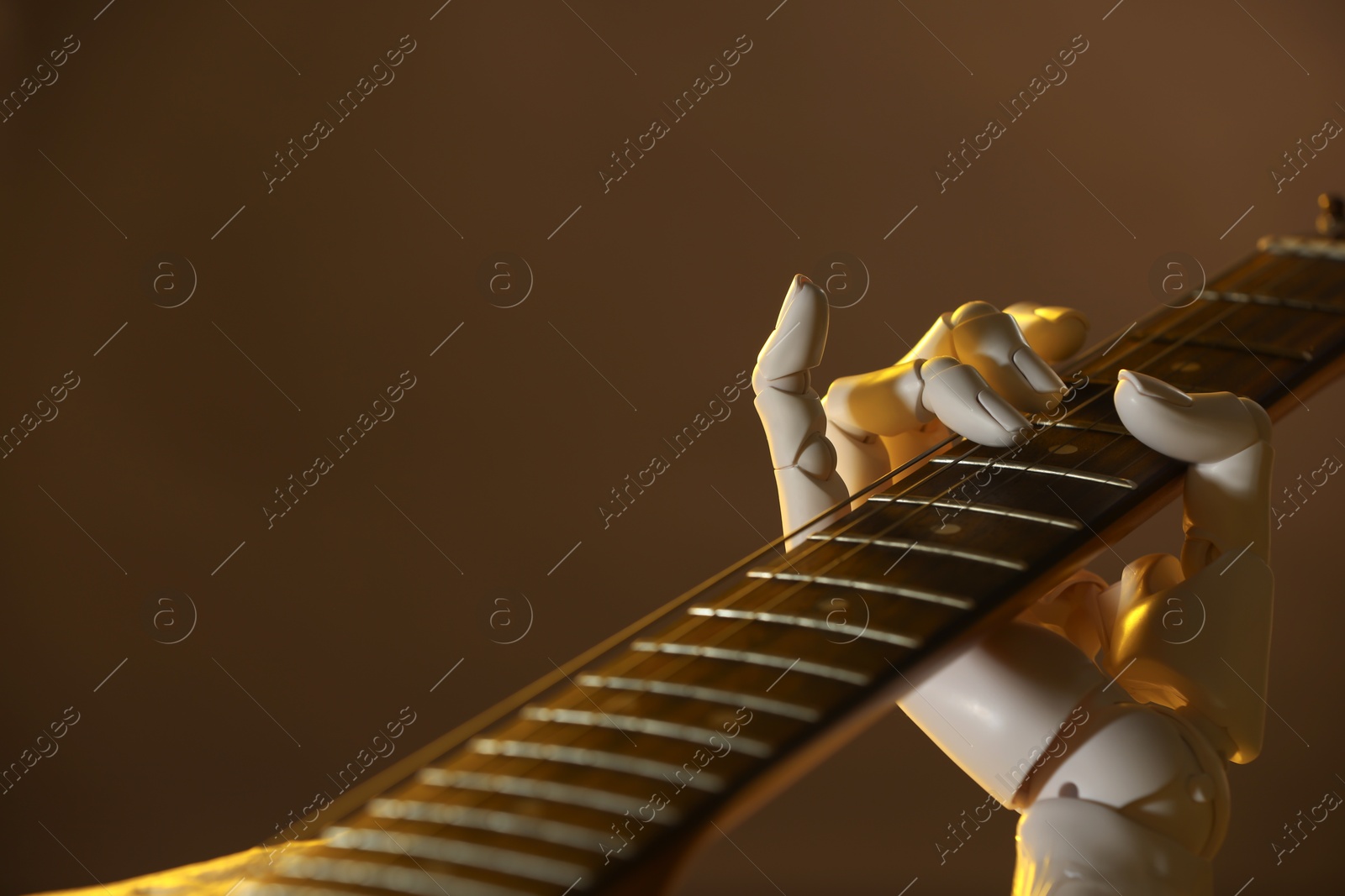 Photo of Artificial intelligence. Robot hand playing guitar on brown background, closeup