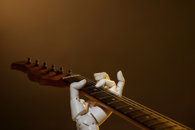 Photo of Artificial intelligence. Robot hand playing guitar on brown background, closeup