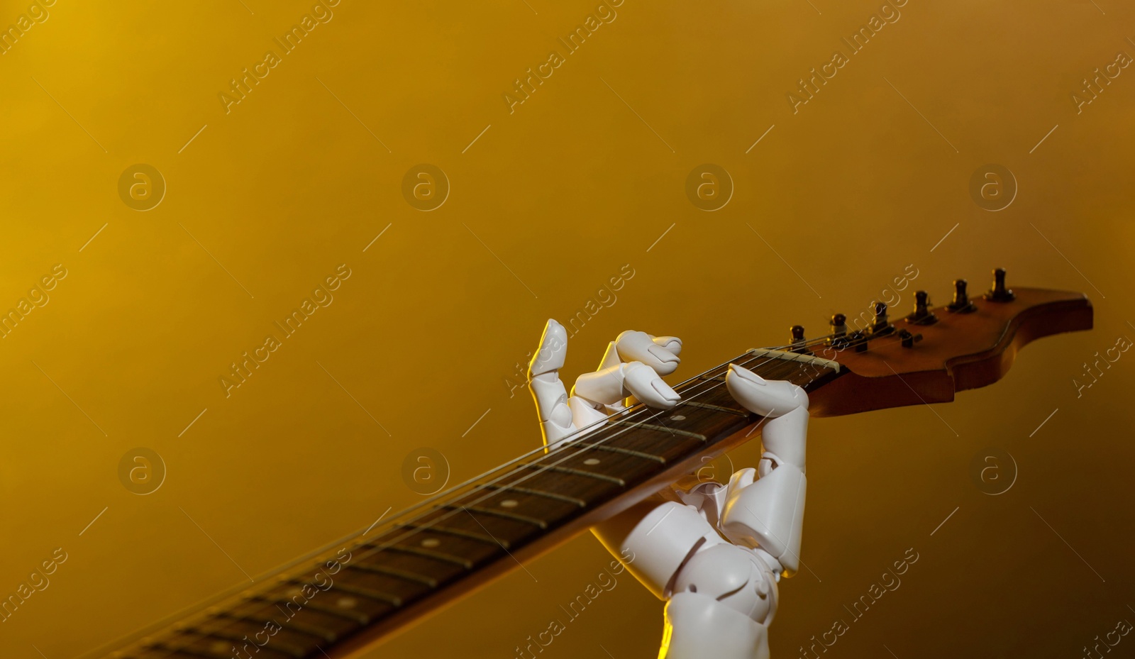 Photo of Artificial intelligence. Robot hand playing guitar on yellow background, closeup