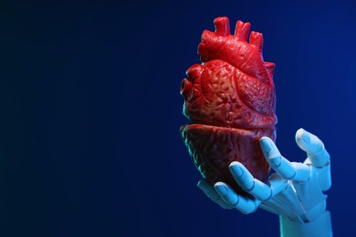 Photo of Artificial intelligence. Robot hand holding model of human heart on blue background, closeup. Space for text