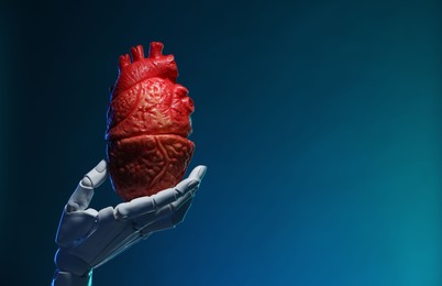 Photo of Artificial intelligence. Robot hand holding model of human heart on blue background, closeup. Space for text