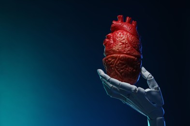 Photo of Artificial intelligence. Robot hand holding model of human heart on blue background, closeup. Space for text