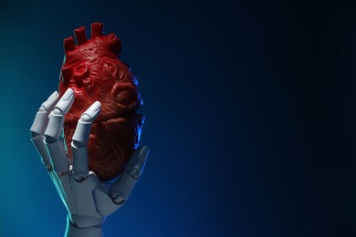 Photo of Artificial intelligence. Robot hand holding model of human heart on dark blue background, closeup. Space for text