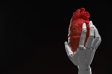 Photo of Artificial intelligence. Robot hand holding model of human heart on black background, closeup. Space for text