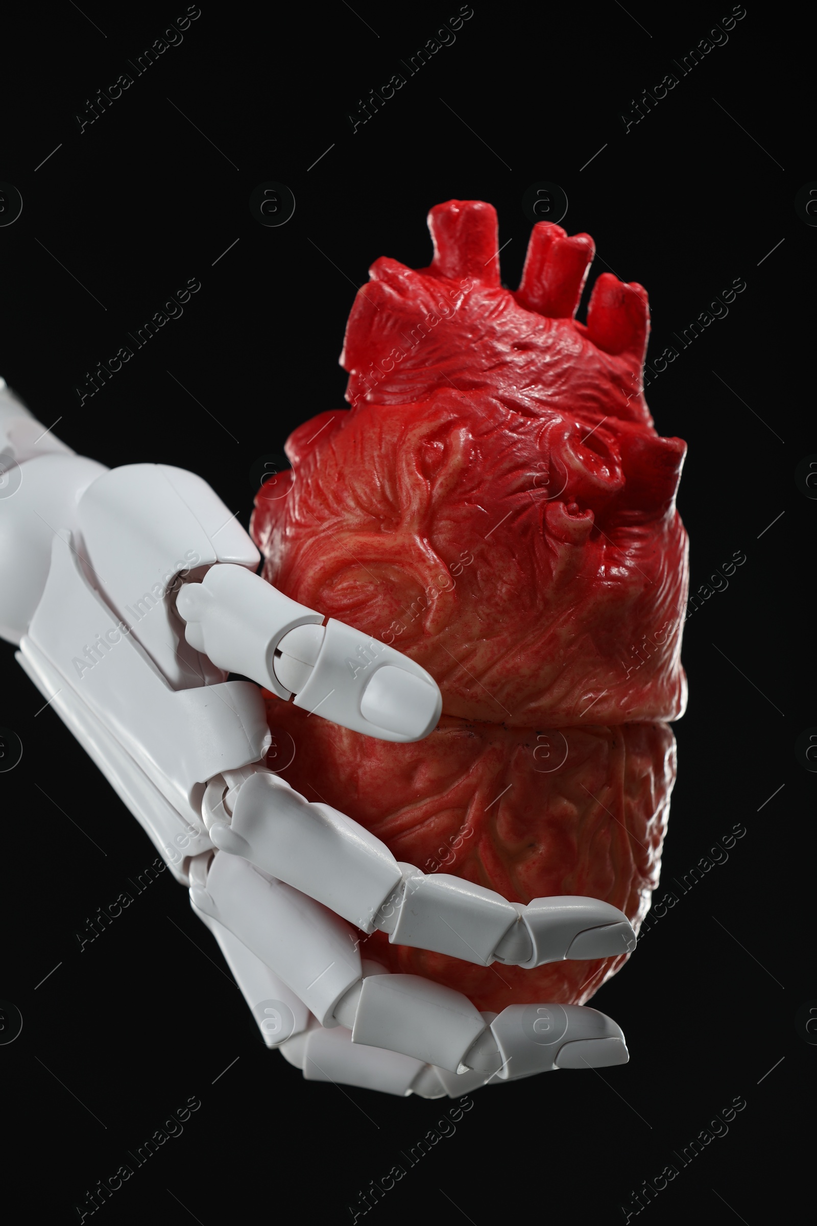 Photo of Artificial intelligence. Robot hand holding model of human heart on black background, closeup