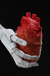 Photo of Artificial intelligence. Robot hand holding model of human heart on black background, closeup