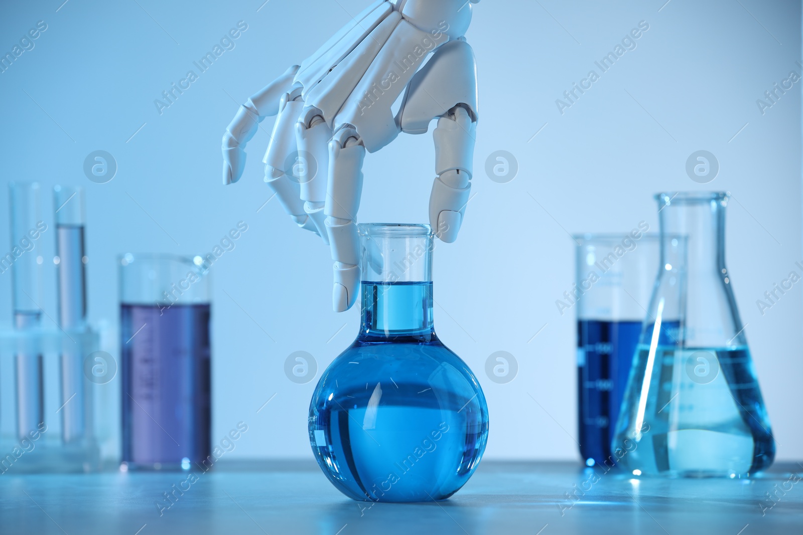 Photo of Artificial intelligence. Robot hand with flask at table in blue light, closeup