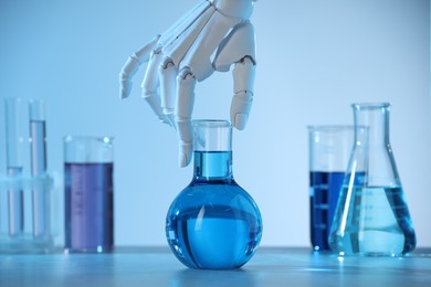 Photo of Artificial intelligence. Robot hand with flask at table in blue light, closeup