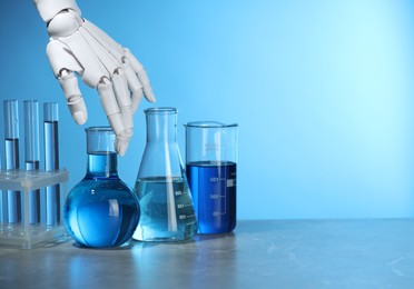 Photo of Artificial intelligence. Robot hand and laboratory glassware with liquids on table against light blue background, space for text