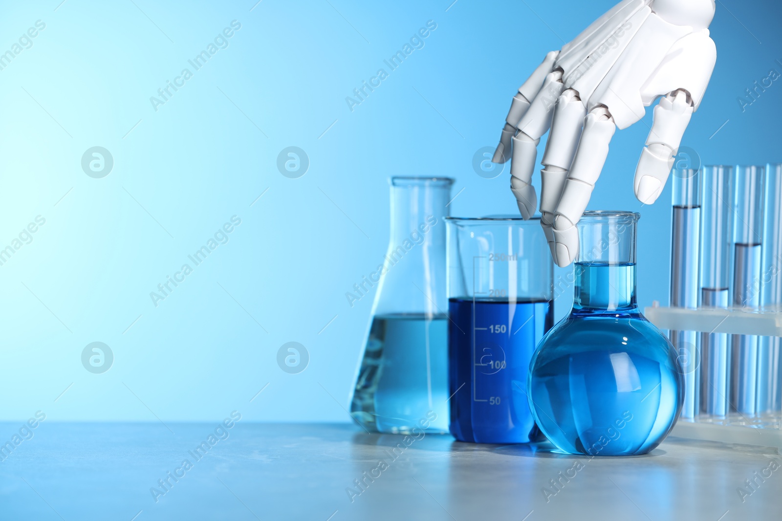 Photo of Artificial intelligence. Robot hand and laboratory glassware with liquids on table against light blue background, space for text