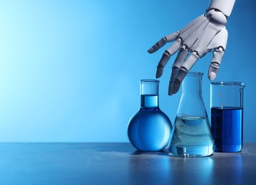 Photo of Artificial intelligence. Robot hand and laboratory glassware with liquids on table against light blue background, space for text