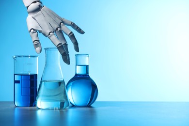 Photo of Artificial intelligence. Robot hand and laboratory glassware with liquids on table against light blue background, space for text