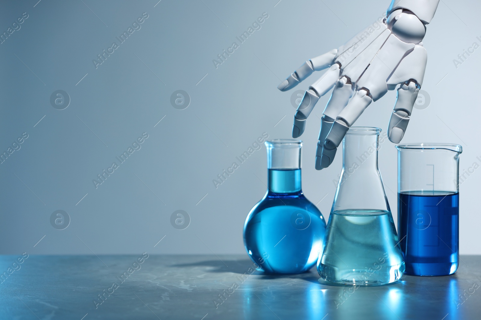 Photo of Artificial intelligence. Robot hand and laboratory glassware with liquids on table against light grey background, space for text