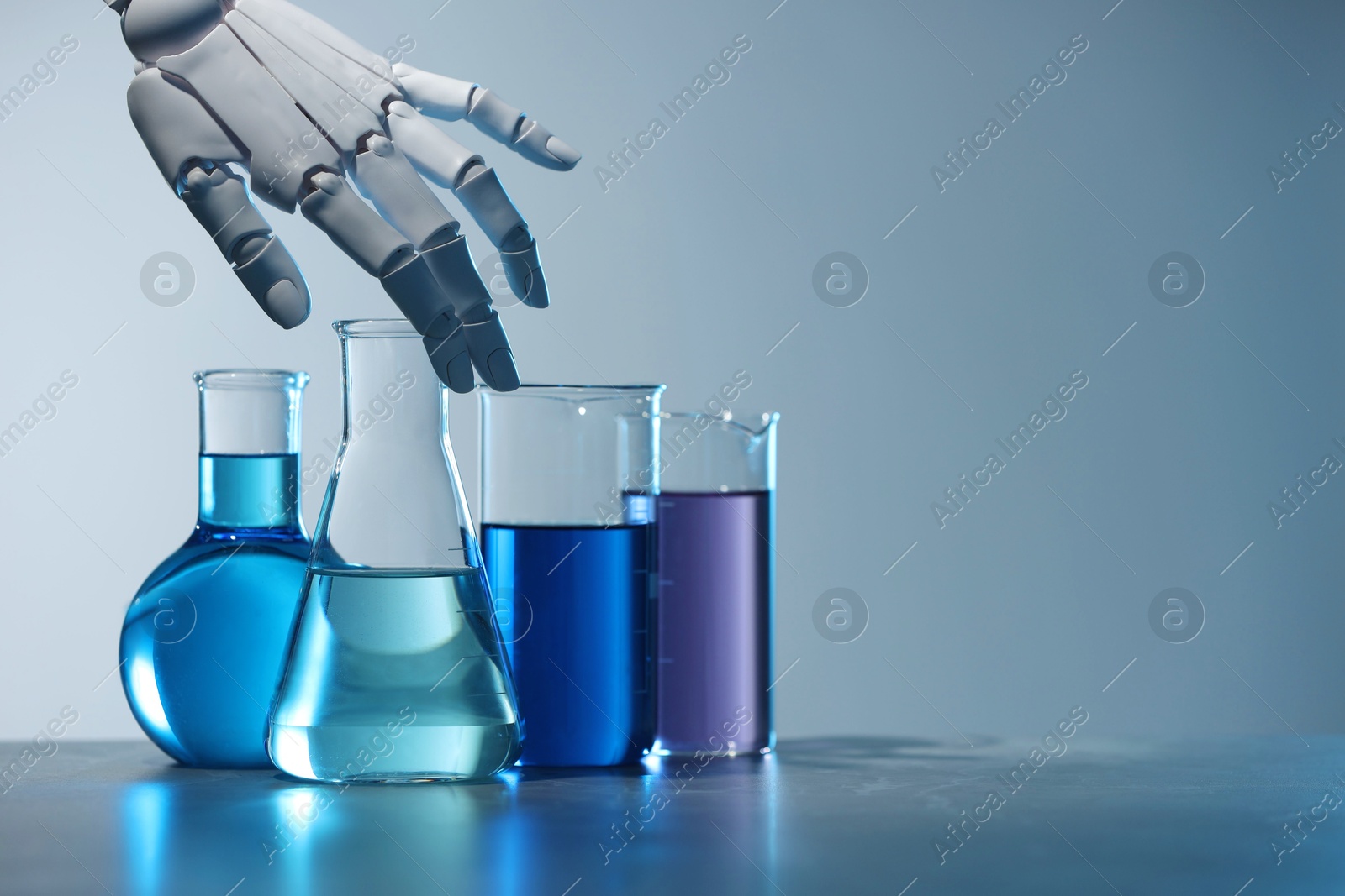 Photo of Artificial intelligence. Robot hand and laboratory glassware with liquids on table against light grey background, space for text